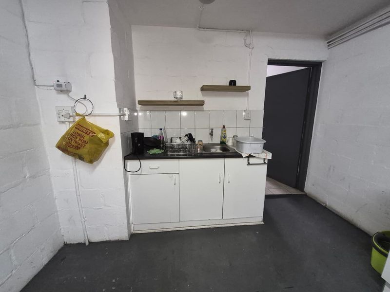 A functional scullery area featuring built-in cabinetry, a stainless steel sink, and tiled splashback, providing essential utility space for the industrial property.