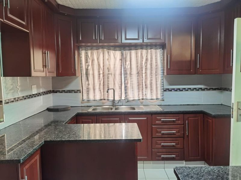 A functional kitchen featuring dark wood cabinetry, granite countertops, a double bowl sink, and a tiled backsplash.
