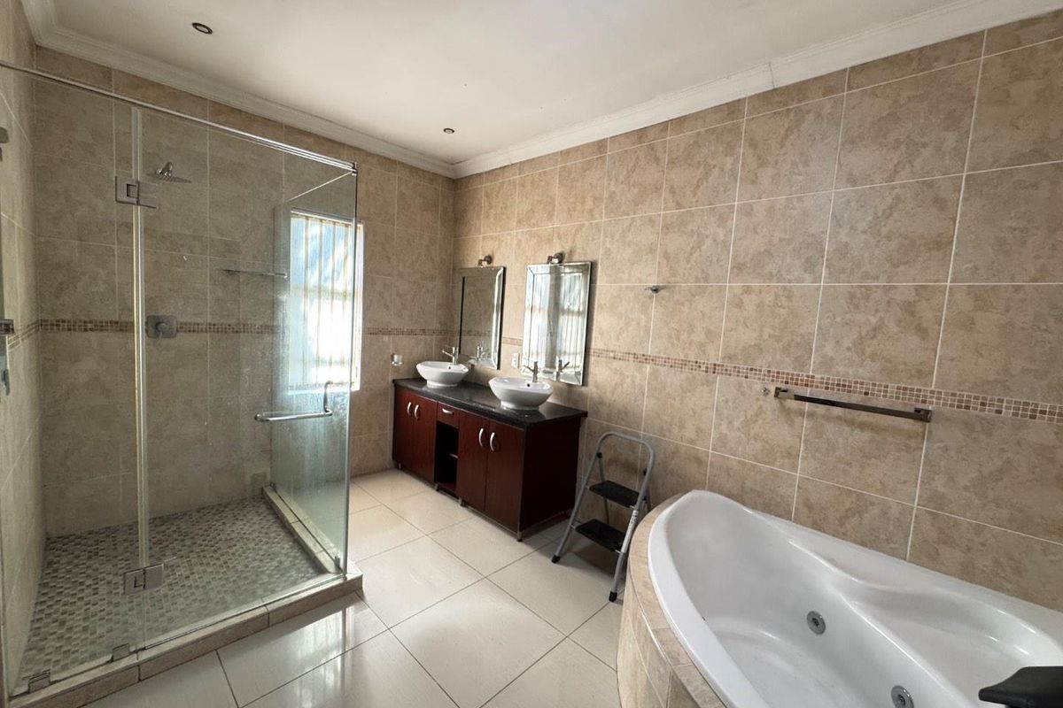 Spacious bathroom featuring a glass-enclosed walk-in shower, a corner jetted bathtub, and a double vanity with granite countertop.
