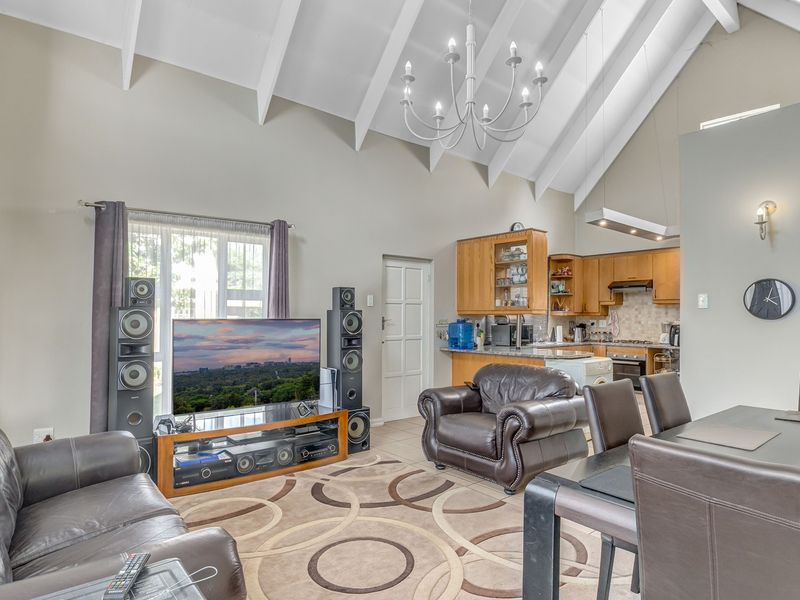 Spacious open-plan living and kitchen area featuring high vaulted ceilings with exposed rafters, a central chandelier, and functional kitchen cabinetry with granite countertops.