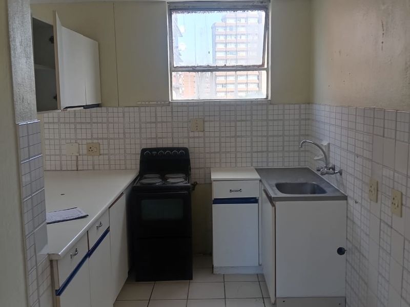 A functional kitchen featuring tiled flooring, a tiled backsplash, built-in cabinetry, and a stainless steel sink, offering a blank canvas for modernization.