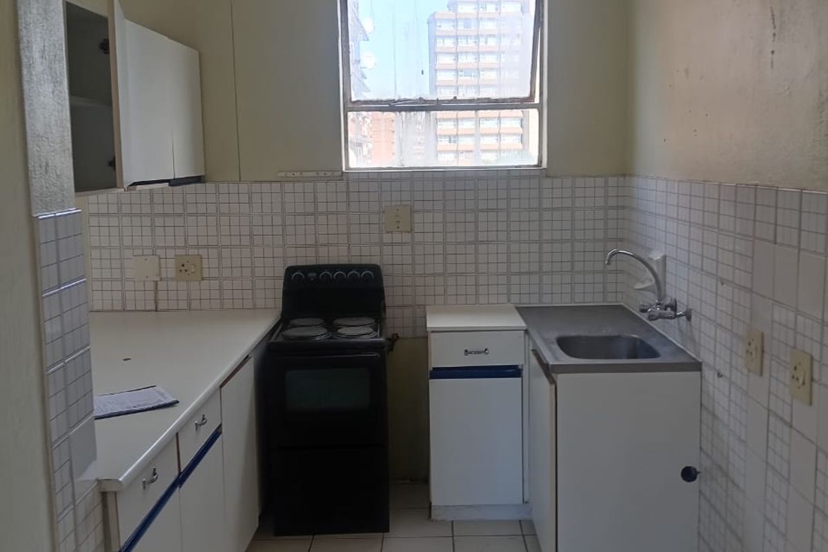 A functional kitchen featuring tiled flooring, a tiled backsplash, built-in cabinetry, and a stainless steel sink, offering a blank canvas for modernization.