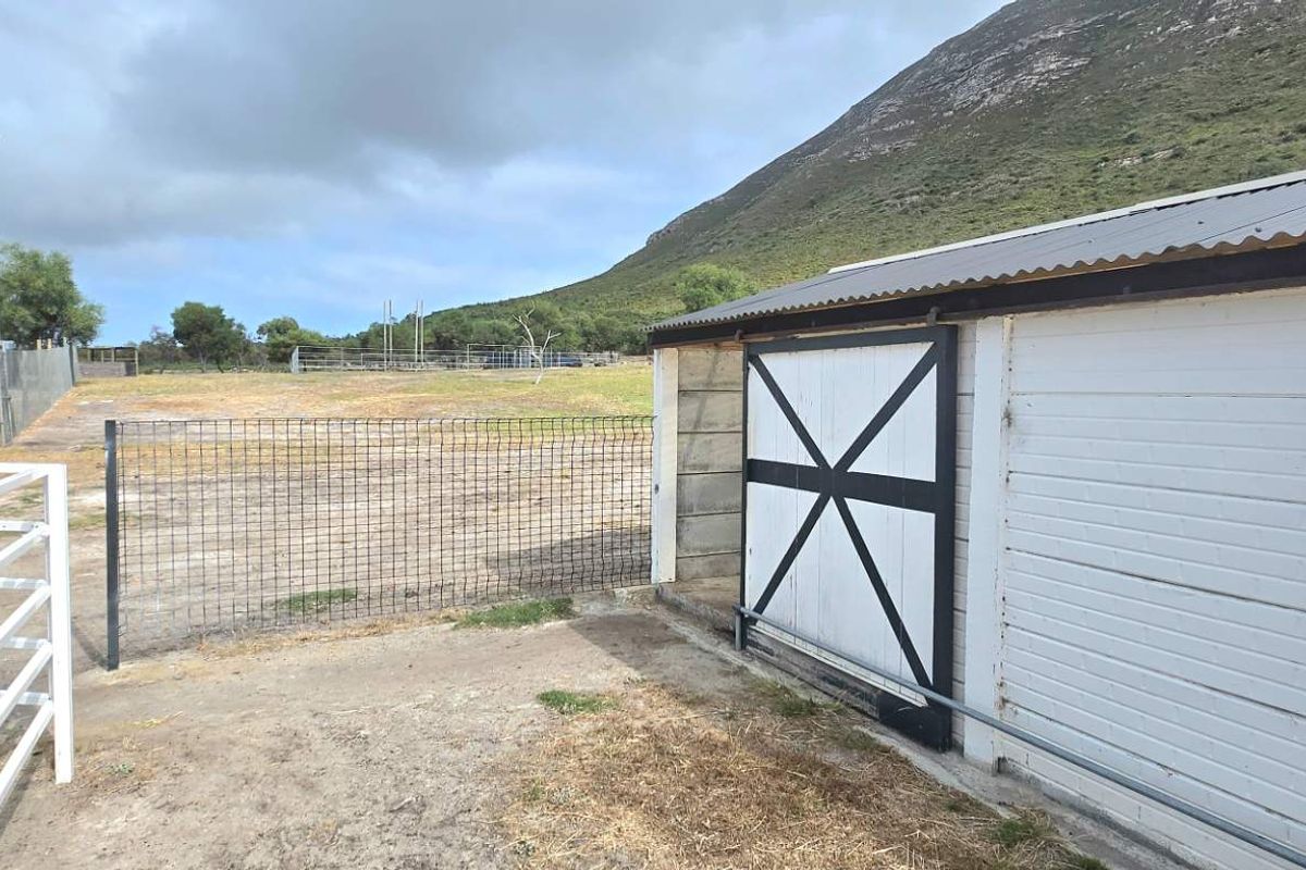 Exterior view of farm outbuildings featuring sliding barn-style doors, metal fencing, and open paddock space against a mountain backdrop.