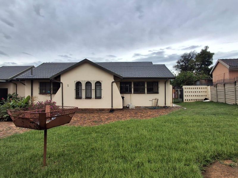 Rear view of the house featuring a paved patio area, lawn, and secure perimeter walling.