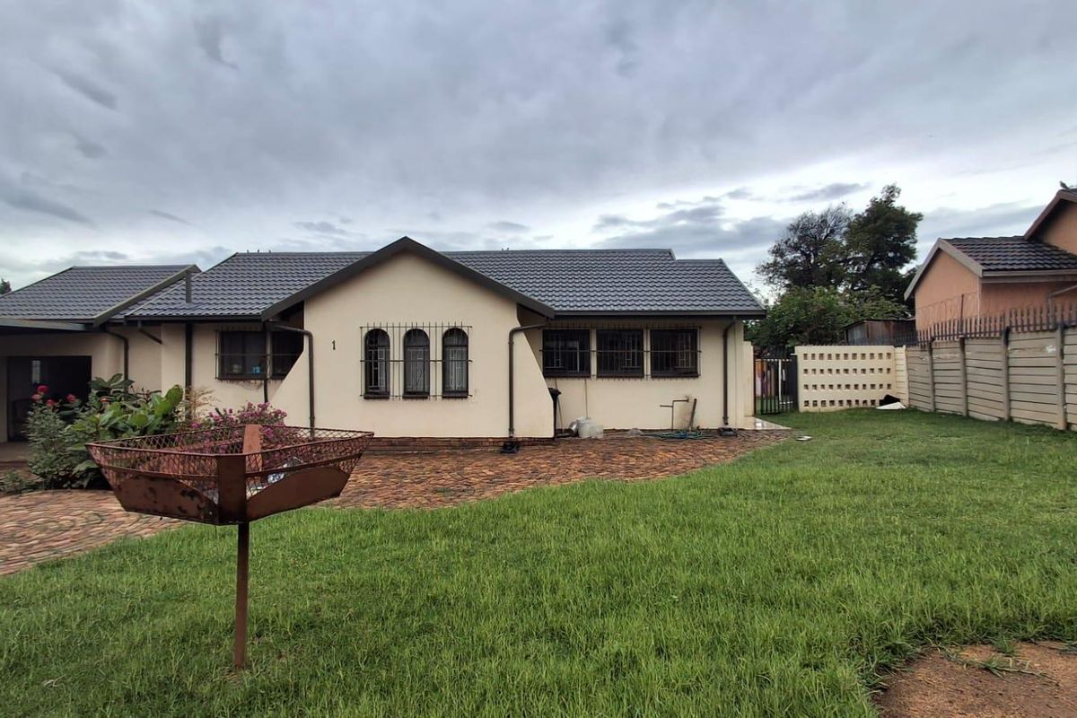 Rear view of the house featuring a paved patio area, lawn, and secure perimeter walling.