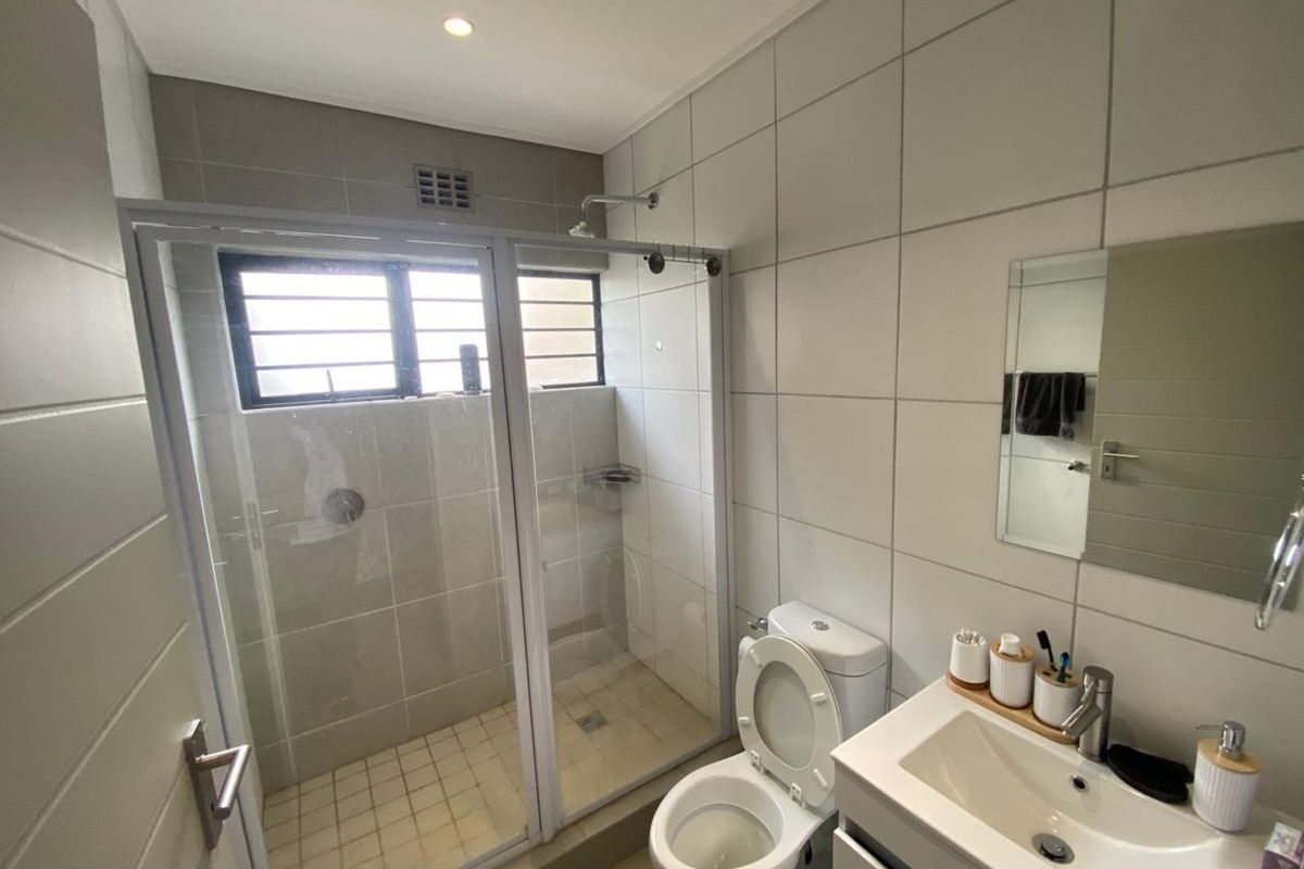 A modern bathroom featuring a glass-enclosed shower, a wall-mounted vanity with a basin, and neutral wall tiling.