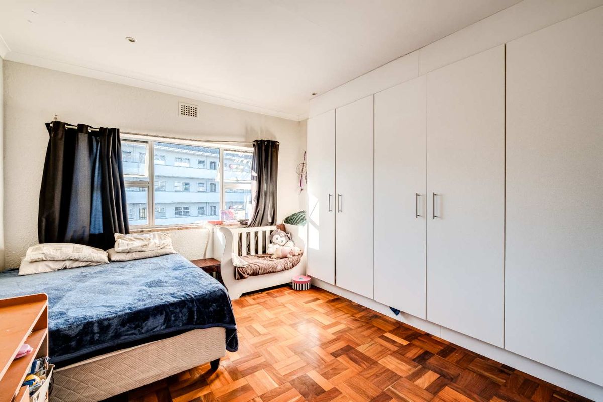 A bedroom featuring classic parquet flooring and extensive floor-to-ceiling built-in white cabinetry, providing ample storage space.