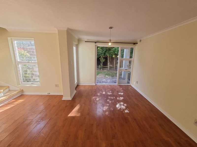 An empty living area featuring laminate flooring, cove cornicing, and a sliding glass door providing direct access to the rear garden.