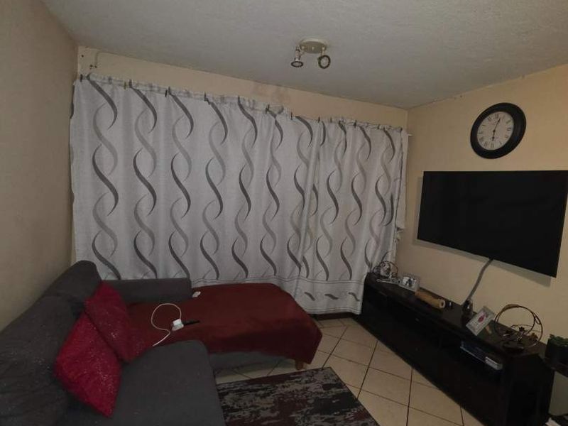 A living room featuring tiled flooring and a ceiling light fixture, currently showing signs of wear on the walls.