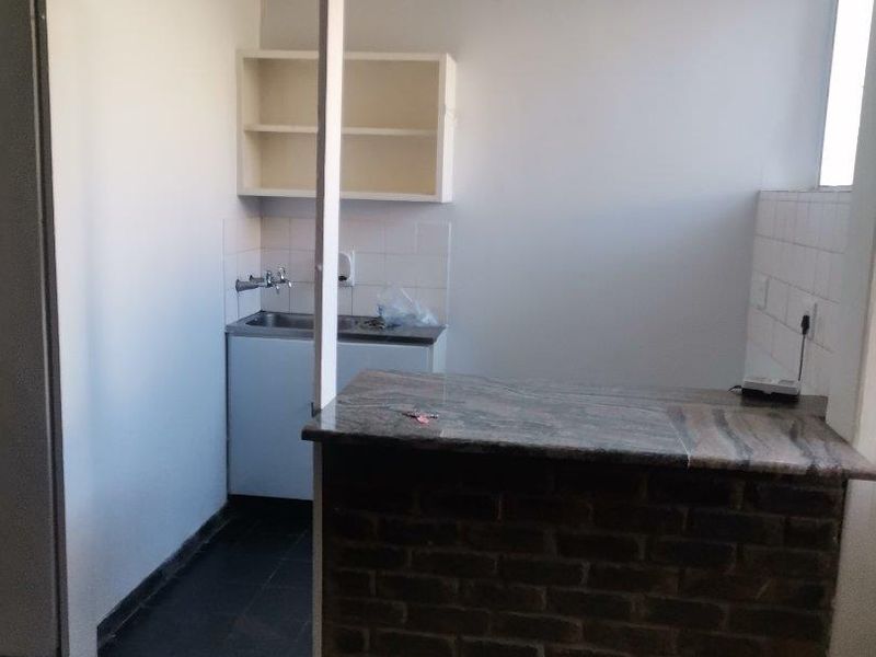 A compact kitchen area featuring a brick breakfast bar, granite countertop, stainless steel sink, and wall-mounted shelving with tiled flooring.