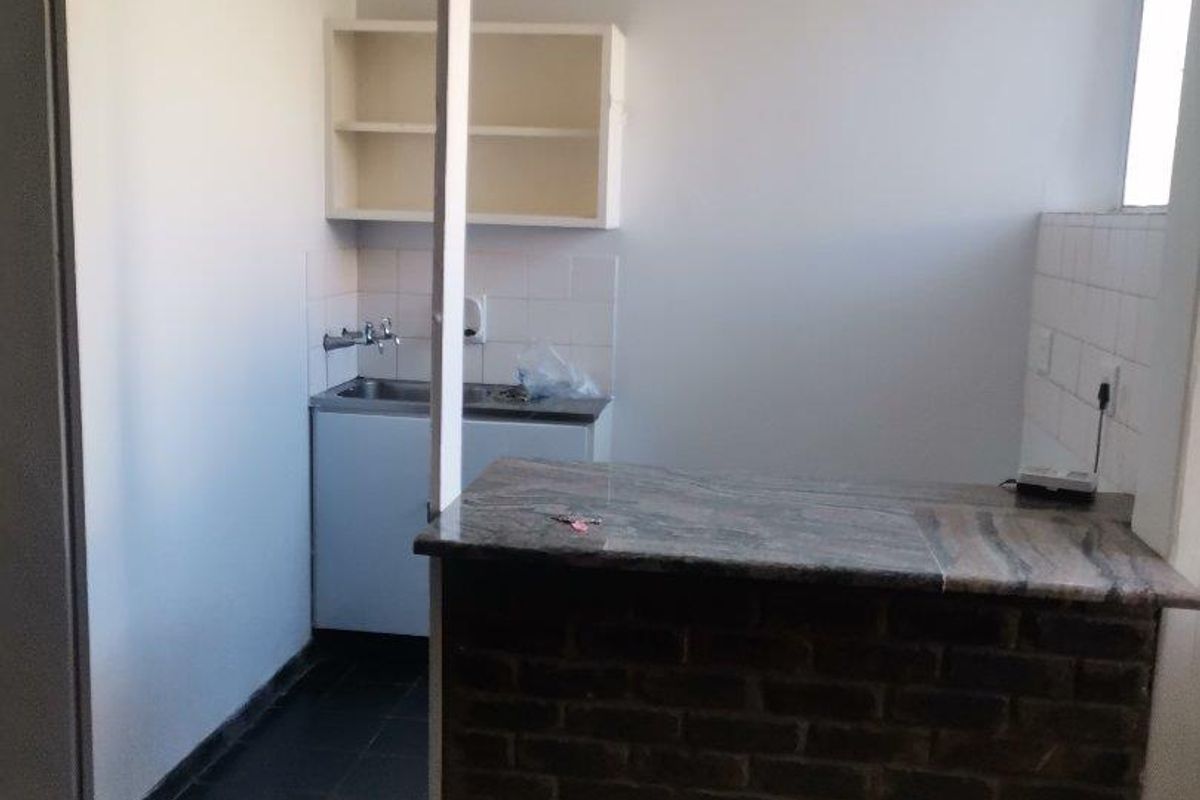 A compact kitchen area featuring a brick breakfast bar, granite countertop, stainless steel sink, and wall-mounted shelving with tiled flooring.