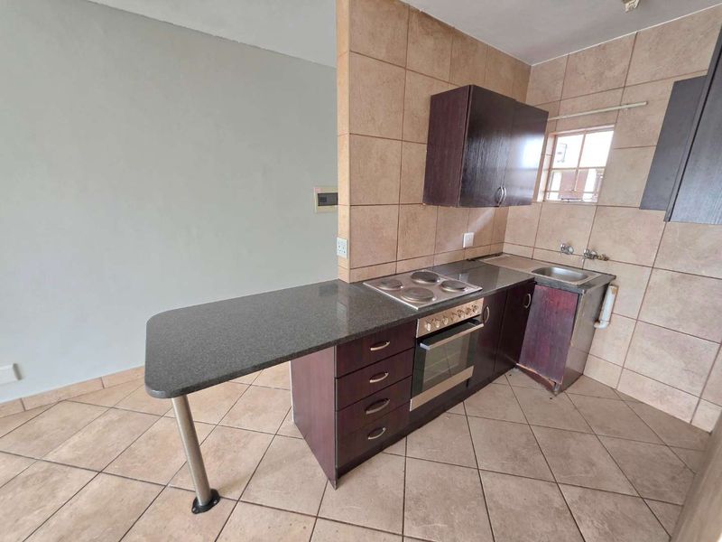 Compact kitchen featuring dark wood cabinetry, granite countertops with a breakfast bar, built-in oven and hob, and tiled finishes throughout.