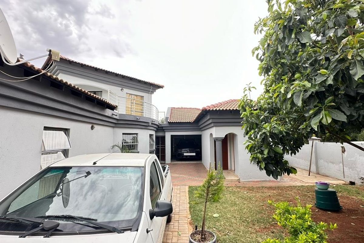 Rear exterior view of the property featuring a paved driveway, garage access, and a small garden area with established trees.