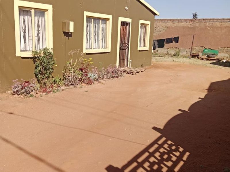 Rear view of a single-story house featuring a dirt yard, security bars on windows, and a perimeter wall.