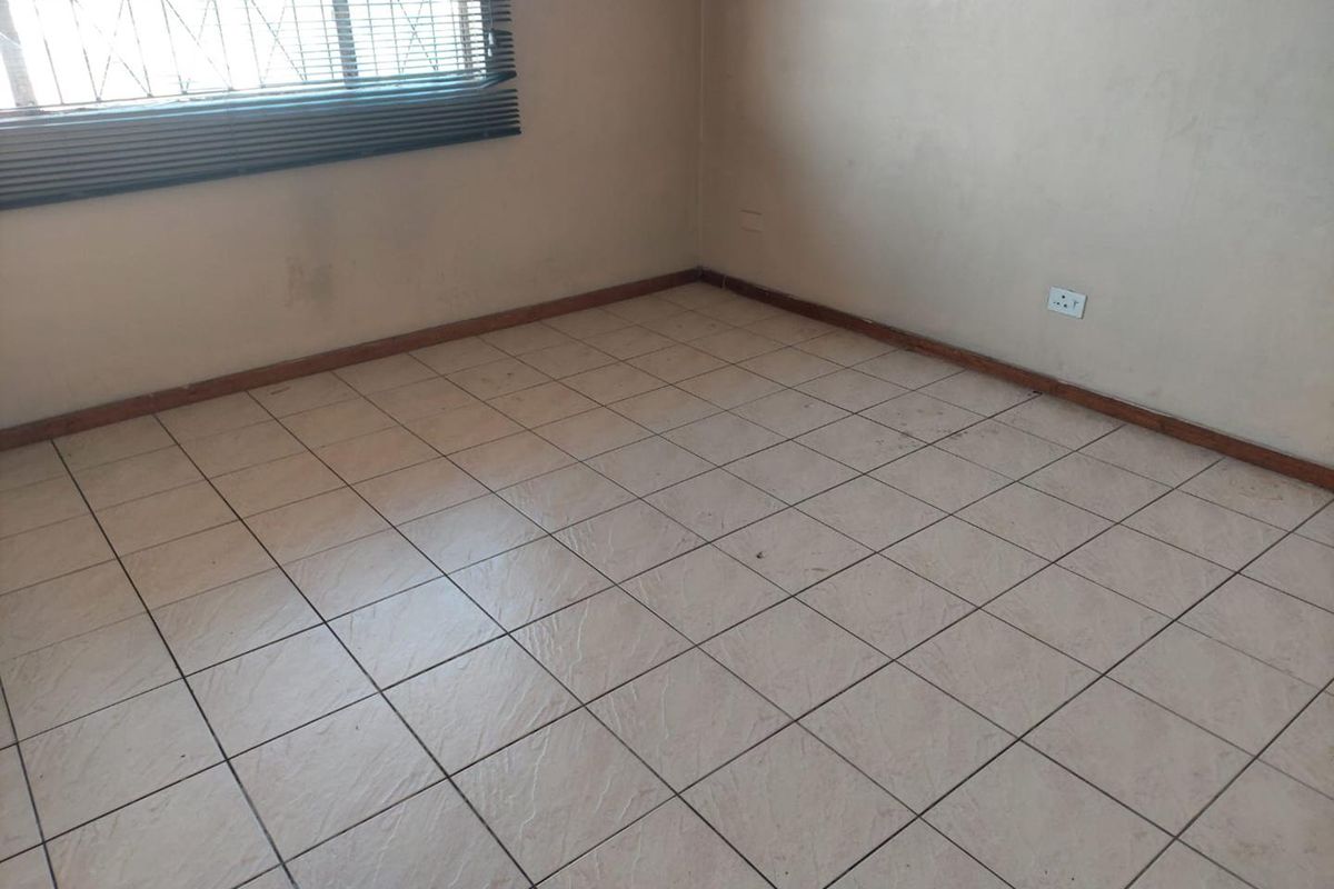 An empty bedroom featuring tiled flooring, security burglar bars on the window, and standard electrical outlets, ready for a fresh coat of paint.