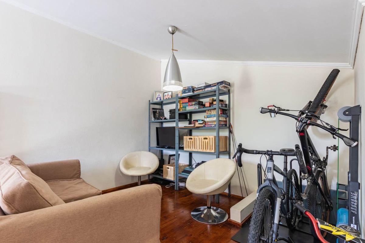 A living room featuring polished hardwood flooring, coving, and a central pendant light fixture, offering a versatile space for relaxation or home office use.