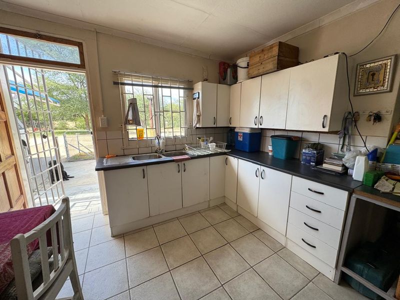 A functional kitchen area featuring white cabinetry, laminate countertops, and a double basin sink, with direct access to the exterior through a security gate.
