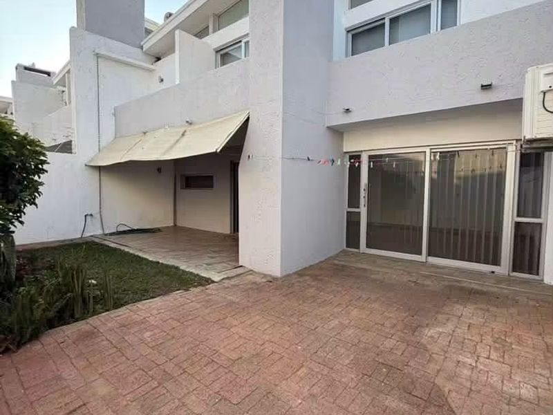 Rear exterior view featuring a brick paved patio, retractable awning, and sliding glass doors leading into the home.