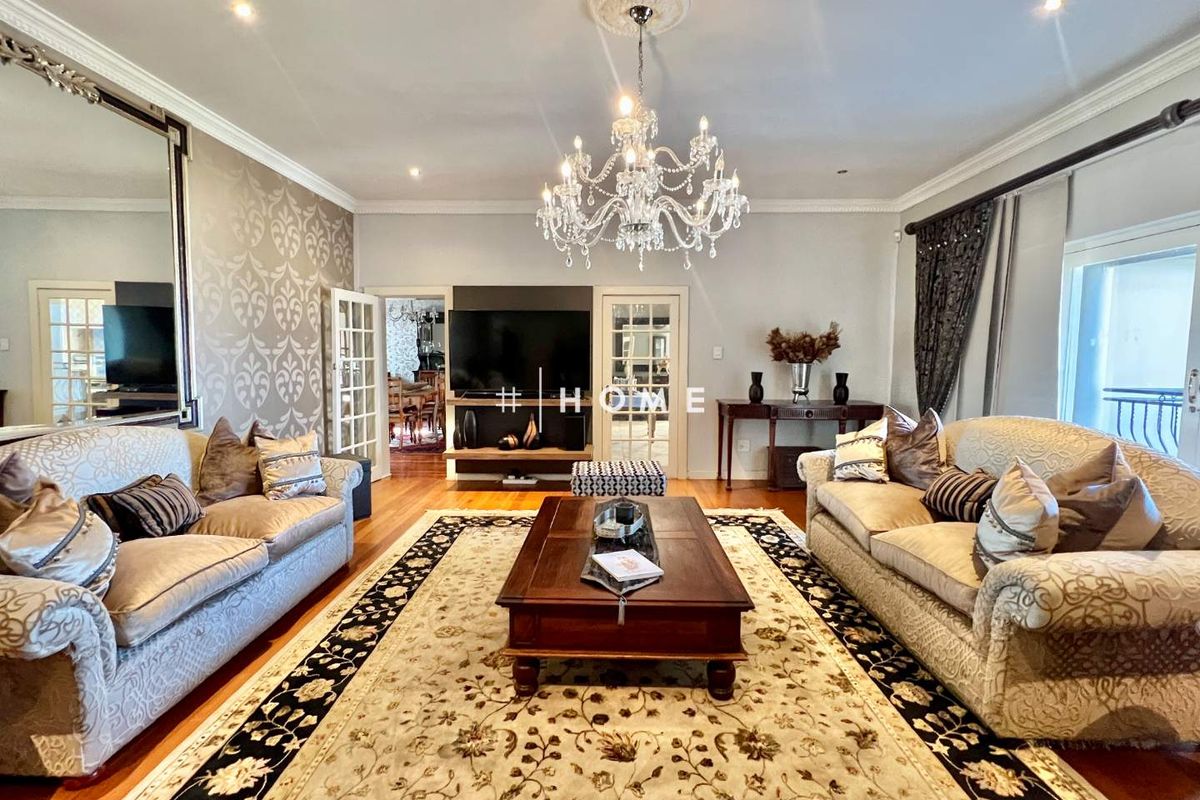 Spacious living room featuring hardwood flooring, decorative ceiling rose with crystal chandelier, and elegant French doors leading to adjacent rooms.