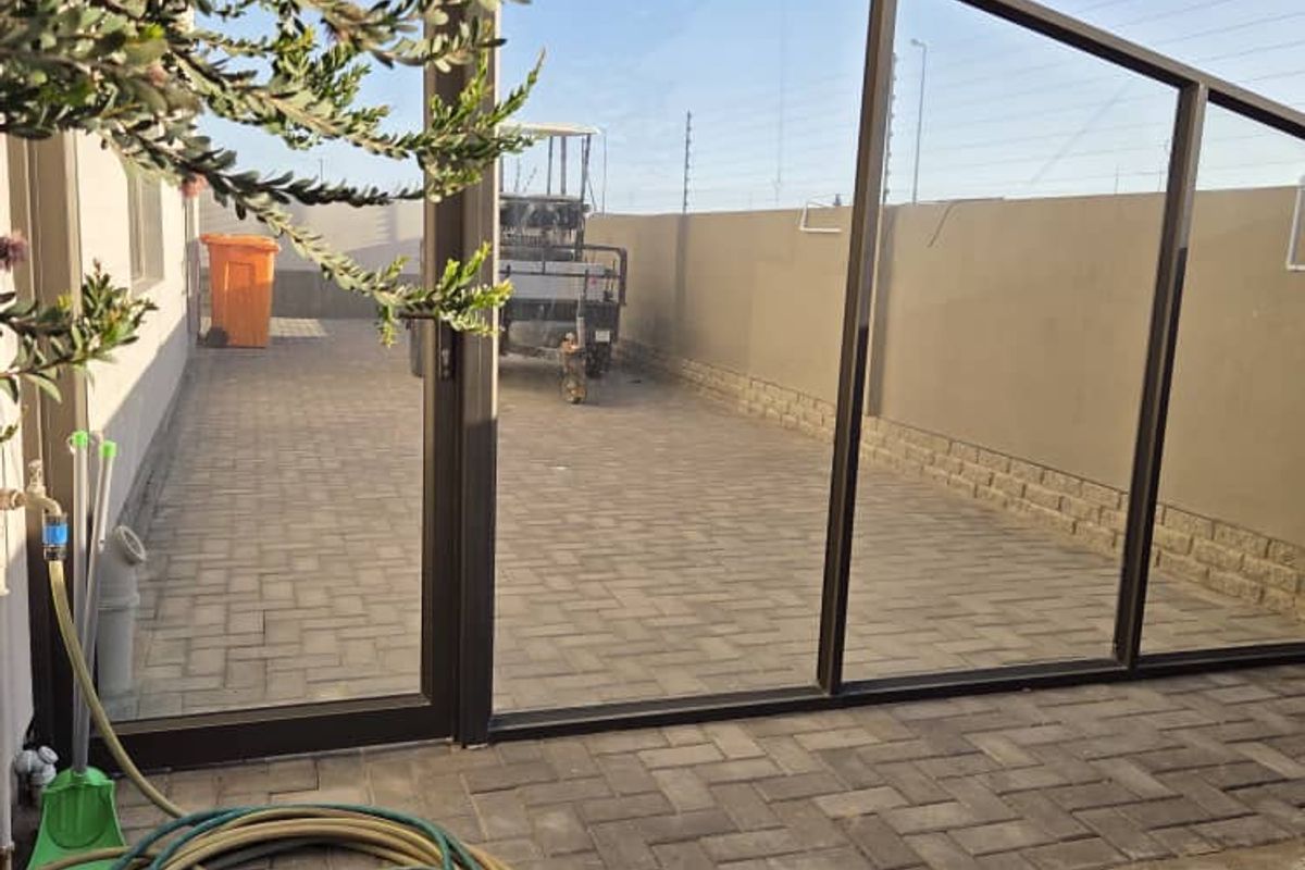 A paved side yard area featuring a large glass partition, perimeter wall, and outdoor tap, providing a functional and low-maintenance exterior space.