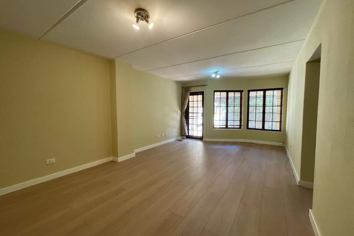 Spacious, empty living area featuring light-toned laminate flooring, neutral wall paint, and access to an outdoor area through a security gate.