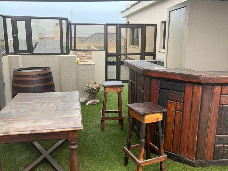 Covered outdoor patio area featuring a built-in bar, artificial turf flooring, and glass balustrades, providing a functional space for outdoor entertaining.