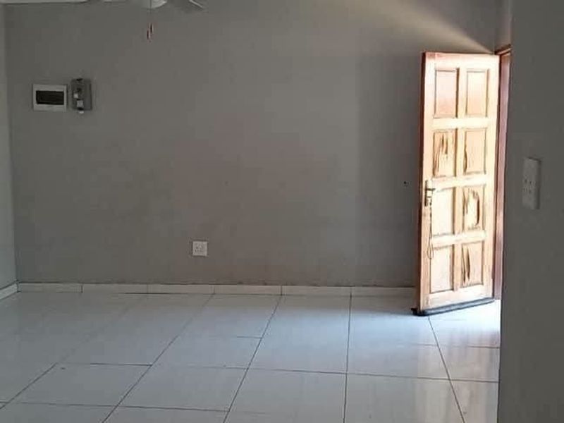 An empty living room featuring tiled flooring, a timber entrance door, and visible wall imperfections requiring maintenance.