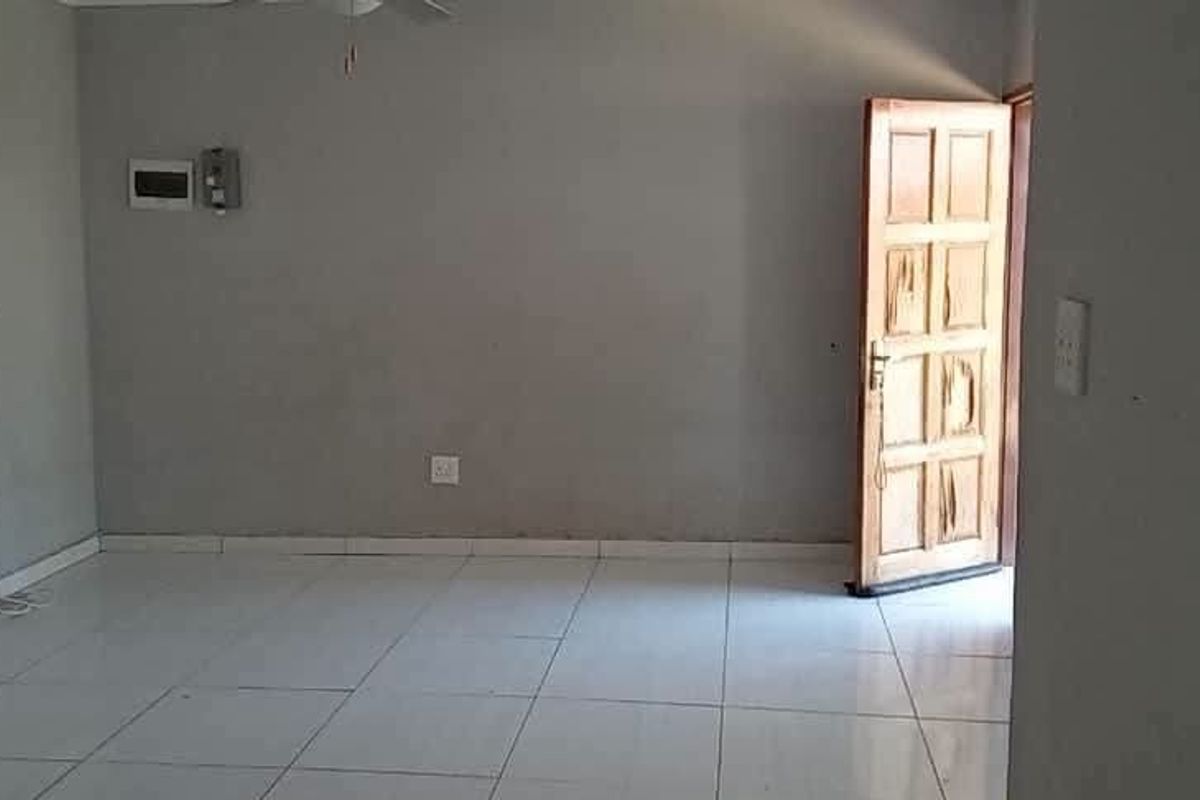 An empty living room featuring tiled flooring, a timber entrance door, and visible wall imperfections requiring maintenance.
