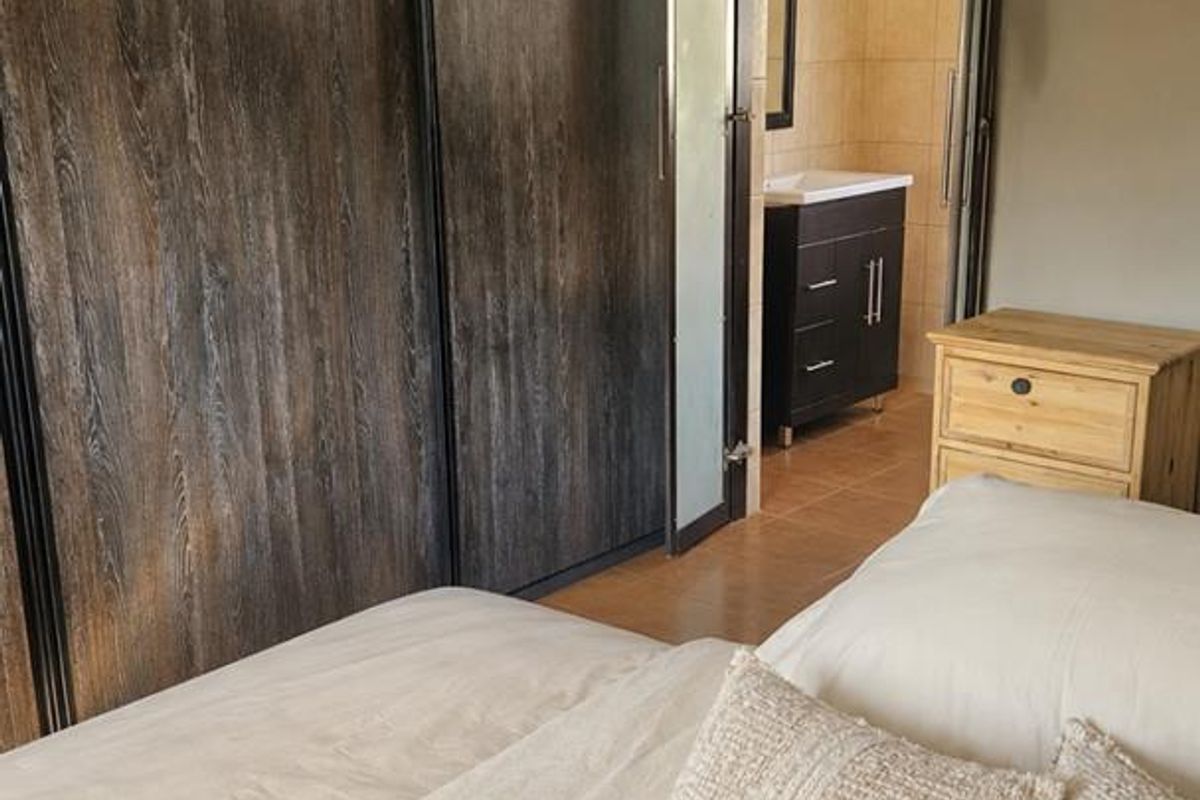 A bedroom featuring large dark wood built-in wardrobes and an adjoining en-suite bathroom with a modern vanity unit.