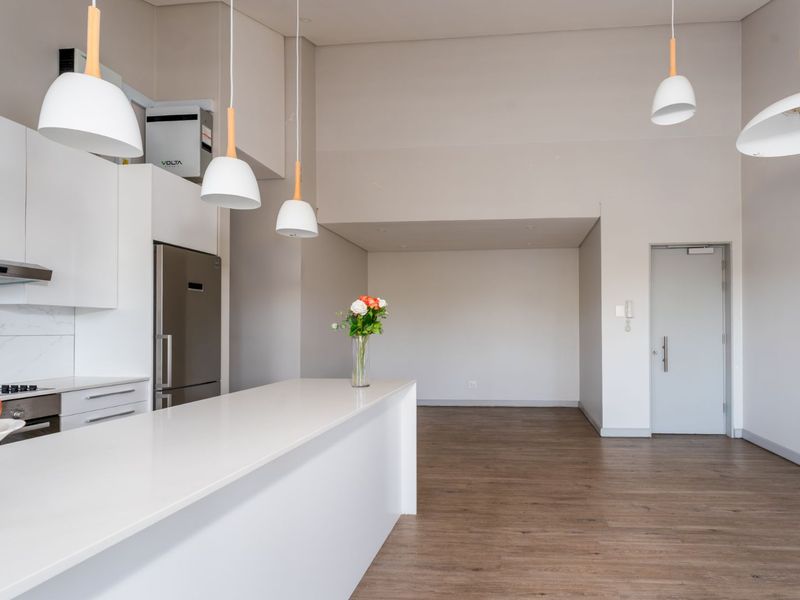 Modern open-plan kitchen and living area featuring sleek white cabinetry, a central island, laminate flooring, and contemporary pendant lighting in a bright, neutral space.