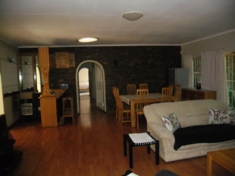 Open plan living and dining area featuring laminate flooring, an exposed brick feature wall, and an arched doorway leading to the rest of the home.