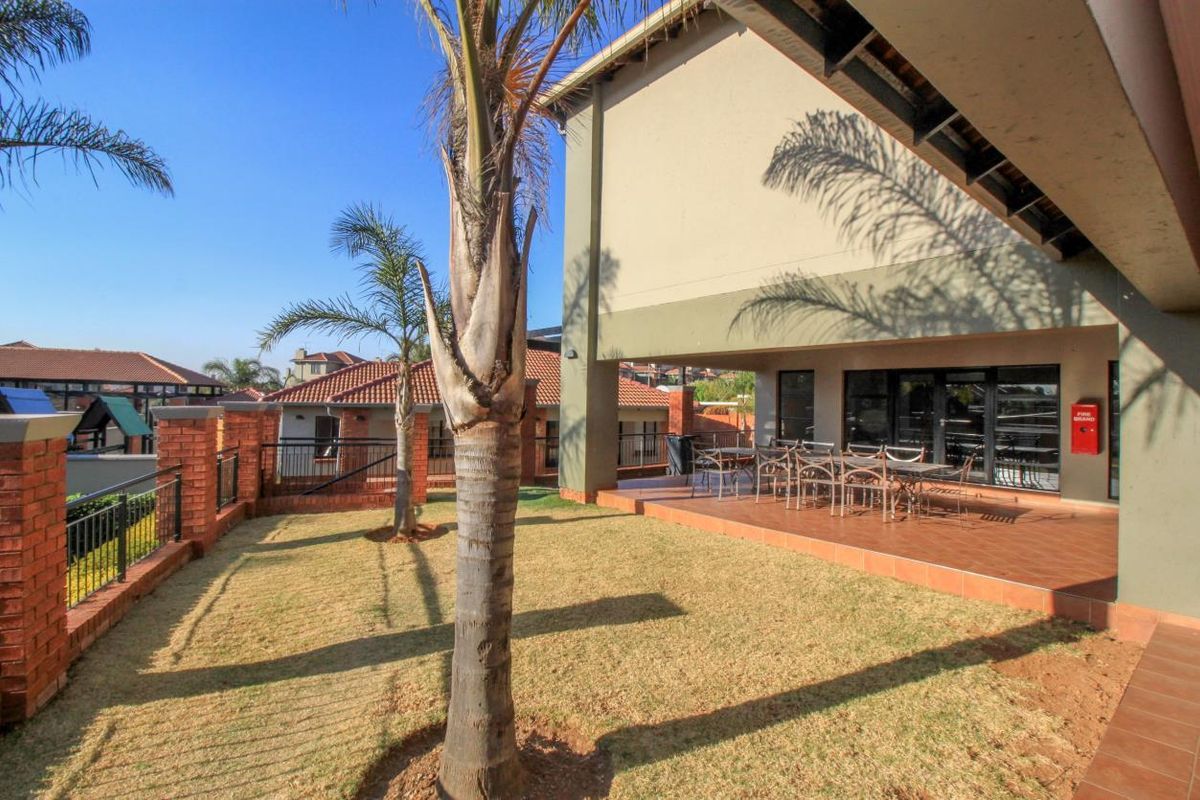 A spacious rear patio with tiled flooring, overlooking a private garden area with brick boundary walls and established palm trees.