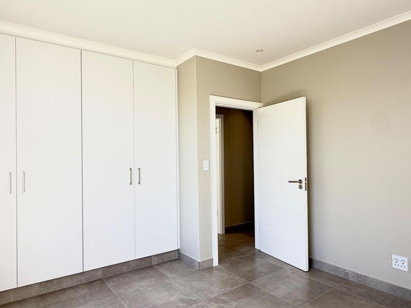 A clean, modern bedroom featuring neutral wall tones, large built-in cupboards, and durable tiled flooring with a contemporary finish.