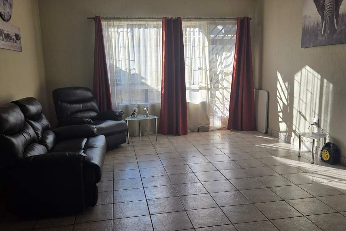 A spacious living room featuring tiled flooring, a ceiling fan, and large windows with curtains providing natural light.