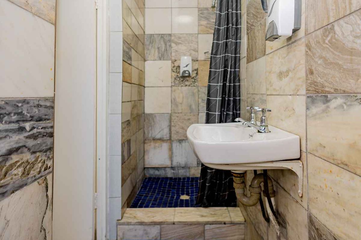 A compact bathroom featuring a wall-mounted basin, exposed plumbing, and a tiled shower enclosure with a curtain.