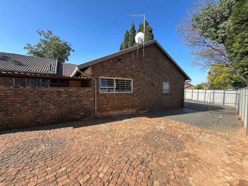 Rear exterior view of the property featuring a face brick facade, paved driveway area, and secure metal gate access.