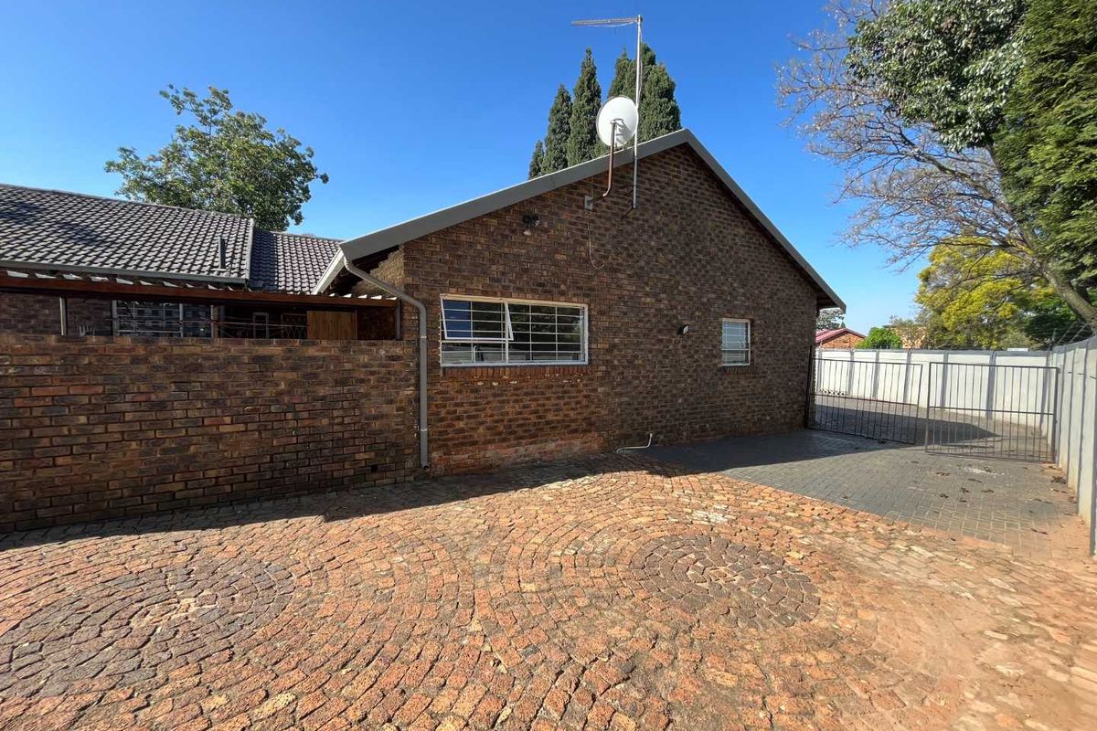 Rear exterior view of the property featuring a face brick facade, paved driveway area, and secure metal gate access.
