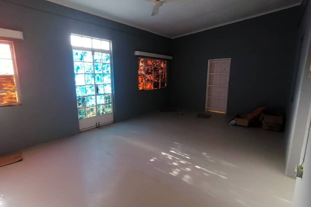 A spacious, empty living room featuring grey walls, a ceiling fan, and multiple windows with decorative glass panes.