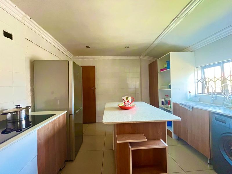 A functional kitchen featuring a central island, tiled backsplash, and built-in cabinetry, offering a practical layout with potential for cosmetic updates.
