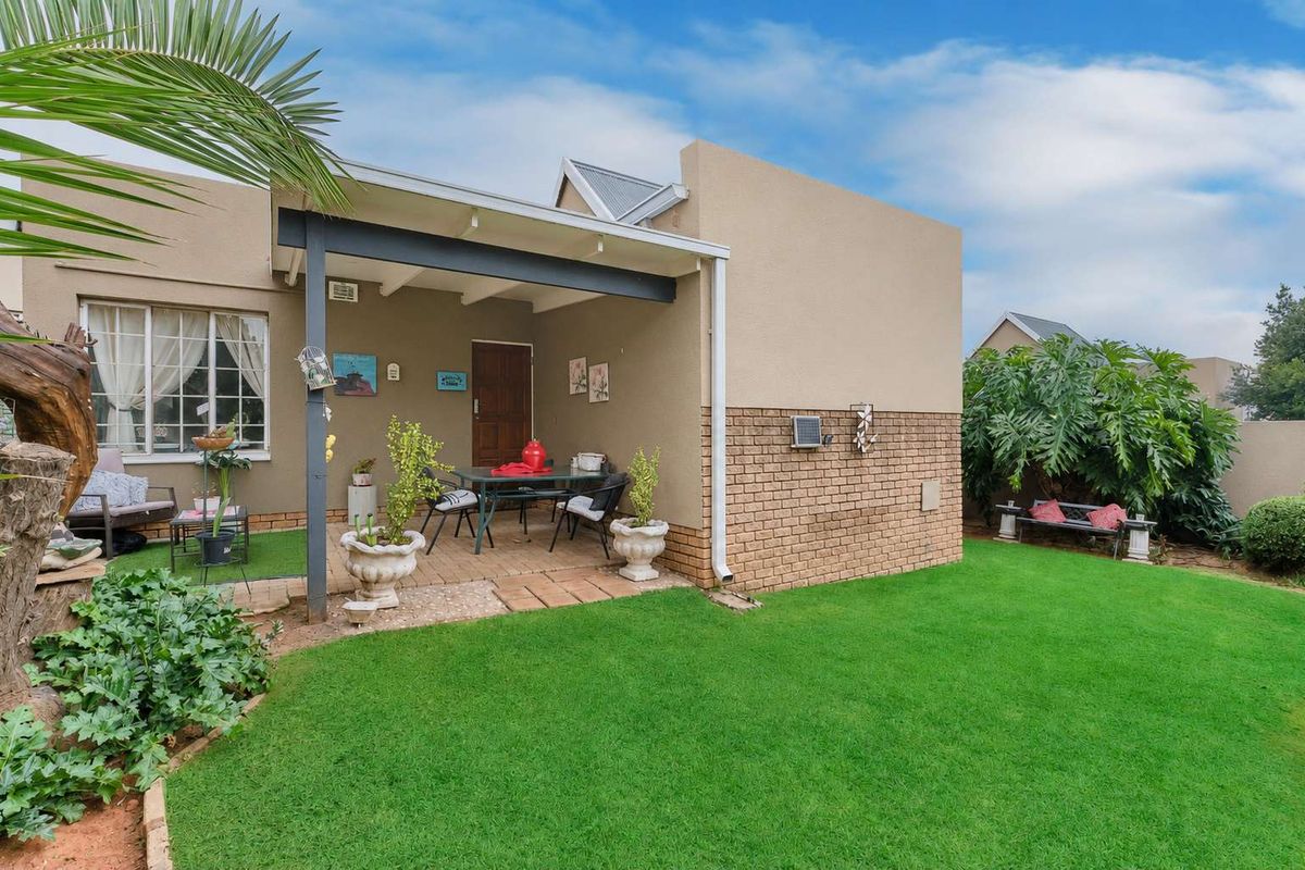 A private rear garden featuring a covered patio area with brick paving, adjacent to a well-maintained lawn and established garden beds.