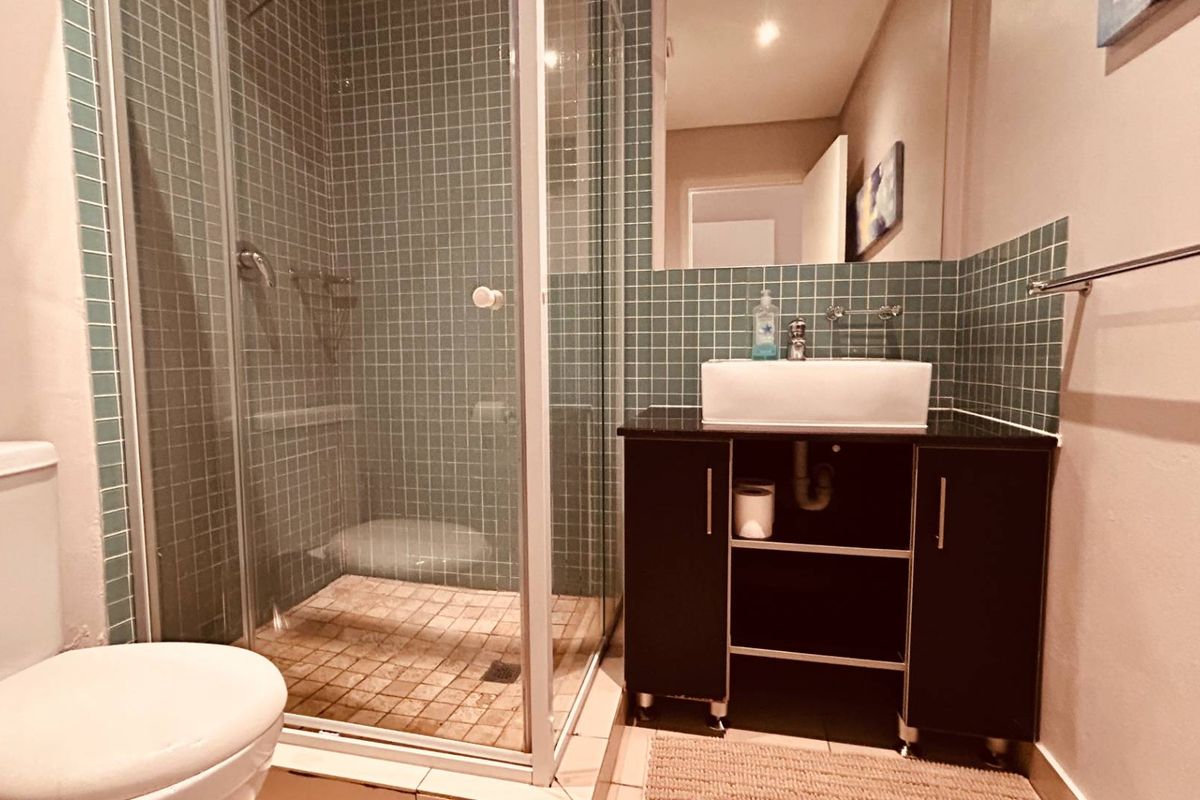 A functional bathroom featuring a glass-enclosed shower with mosaic tiling, a modern vessel sink on a vanity cabinet, and a wall-mounted mirror.
