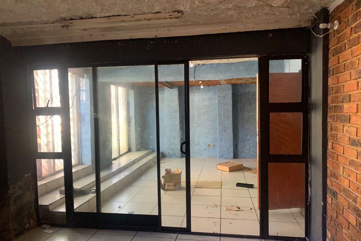 An interior view of a vacant room featuring large sliding glass doors, exposed brickwork, and tiled flooring, requiring significant renovation and cosmetic updates.
