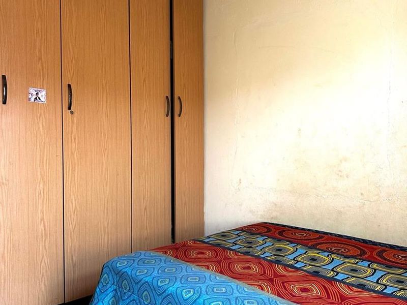 A bedroom featuring built-in wooden cupboards, tiled flooring, and a textured ceiling. The room requires cosmetic updates to the walls and ceiling.
