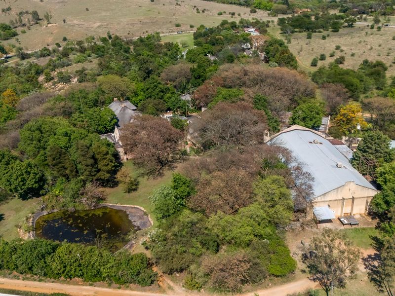 Aerial view of a small holding property featuring a large warehouse structure, a natural pond, and extensive mature landscaping.