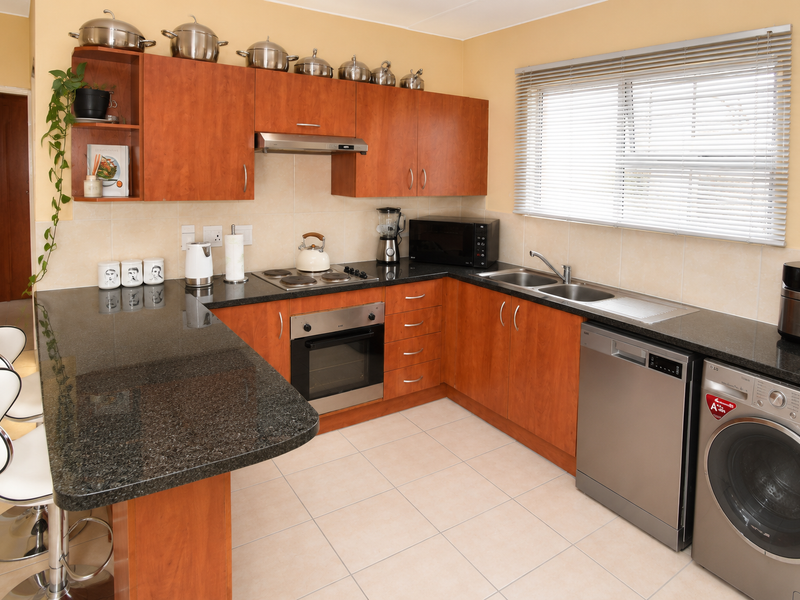 A functional kitchen featuring granite countertops, wood-veneer cabinetry, built-in oven, electric hob, and integrated space for laundry appliances.