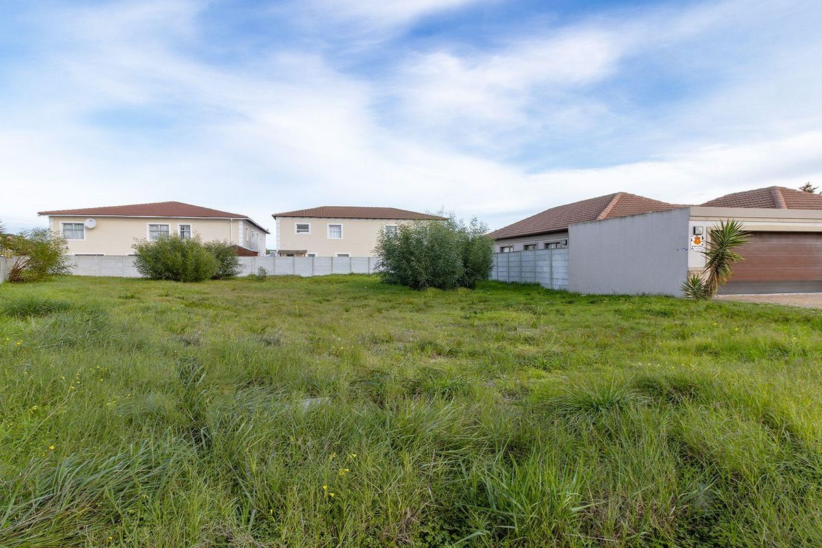 A vacant residential plot featuring grassed land and enclosed by precast concrete boundary walls, situated in a developed suburban neighborhood.