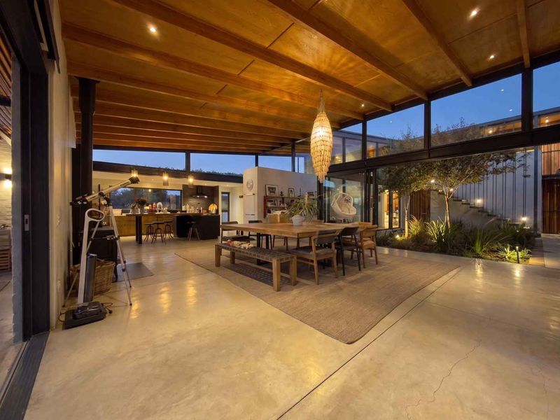 Spacious open-plan living and dining area featuring polished concrete floors, exposed timber ceilings, and floor-to-ceiling glass walls overlooking a private internal courtyard.