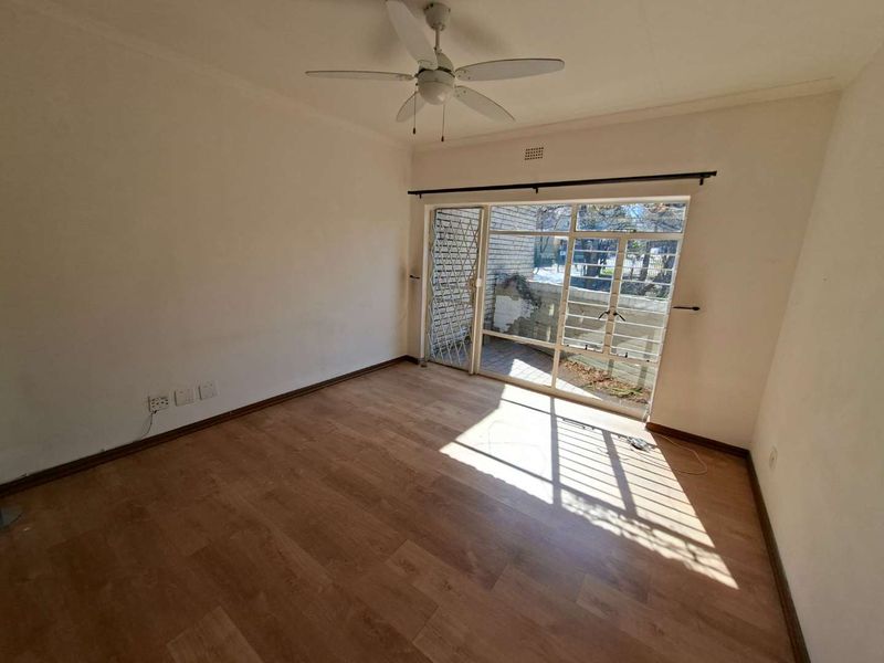 An empty bedroom featuring laminate flooring, a ceiling fan, and a sliding door with a security gate leading to an outdoor area.