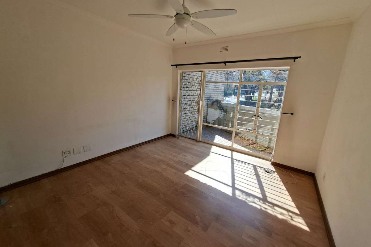 An empty bedroom featuring laminate flooring, a ceiling fan, and a sliding door with a security gate leading to an outdoor area.
