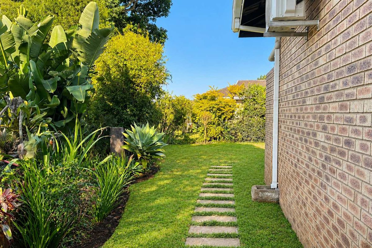A well-maintained rear garden area featuring a brick townhouse facade, a stone paver pathway, and established landscaping.